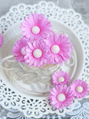 Pink artificial flowers with white centers on a decorative white plate.