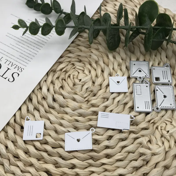 Decorative metal charms shaped like envelopes on a textured surface with green leaves.