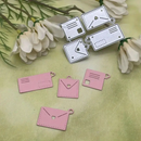 Pink paper cutouts shaped like cards and envelopes on a green surface with flowers.