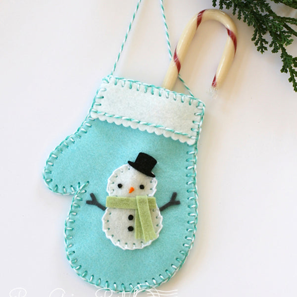 Felt snowman ornament on a light blue background with a candy cane and greenery.