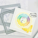 Card with rainbow circular design and butterfly, surrounded by decorative stencils on a marble surface.