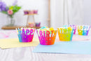 Colorful 'Happy Birthday' cupcake liners on a table with a blurred background