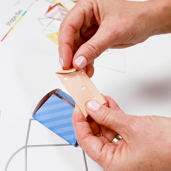 Person applying a small piece of paper with holes to a wooden stick, with a blurred background.