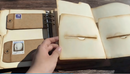 Hand holding a leather-bound notebook with visible stamps on a wooden surface