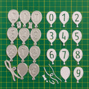 Metal balloon-shaped numbers and letters on a green grid background