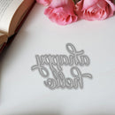 Metallic 'Happy Birthday' cutting die on a white surface with pink roses and an open book.