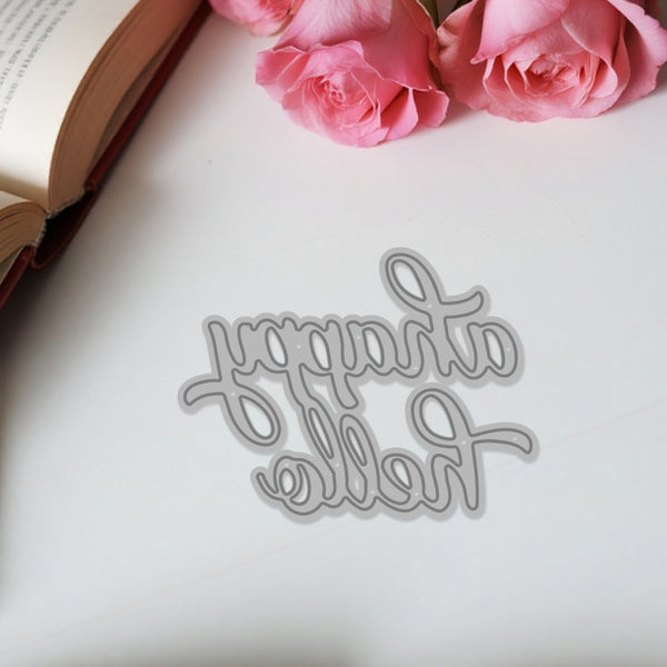 Metallic 'Happy Birthday' cutting die on a white surface with pink roses and an open book.