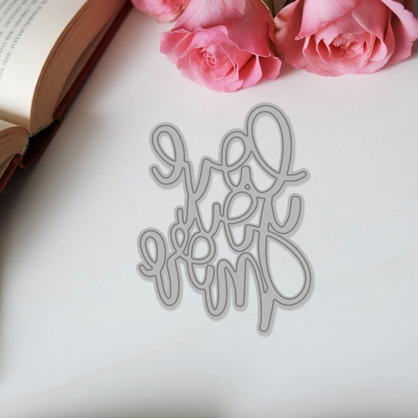 Decorative metal word cutout on a white surface with pink roses and an open book.