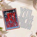 Card with 'Joy to the World' text and a metal cutting die on a light surface with flowers.