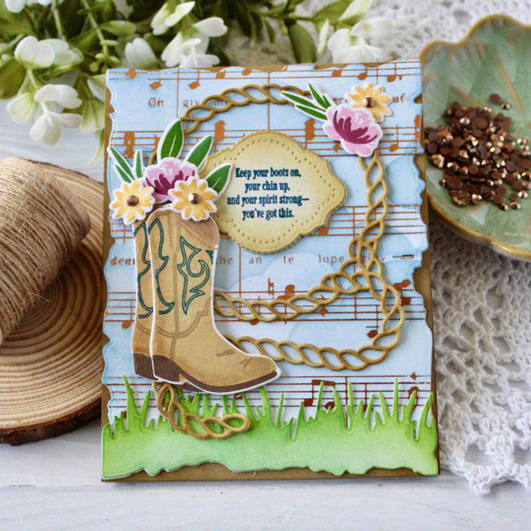 Decorative card with cowboy boot, flowers, and music notes on a white surface with floral and yarn background.