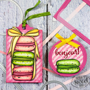 Decorative tags with macaron designs and 'bonjour!' text on a textured surface.