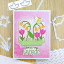 Card with tulips and butterfly design on a pink background, surrounded by die-cutting tools.
