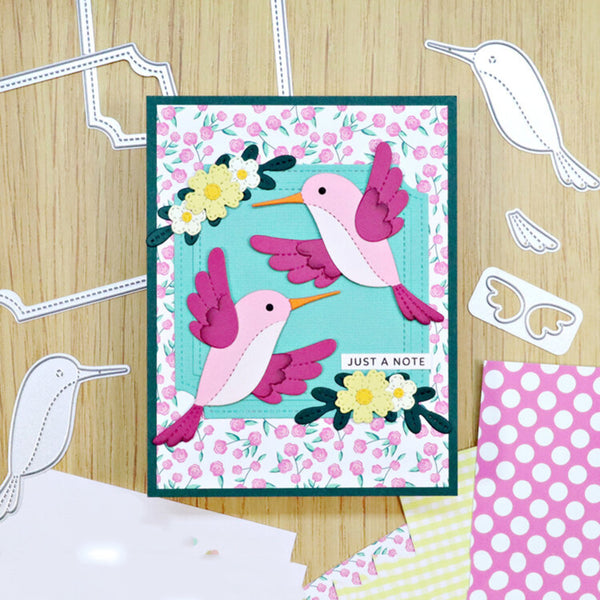 Card with pink and purple hummingbird design on a wooden surface with craft materials.