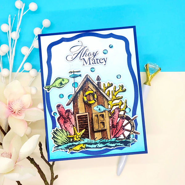Colorful card with a nautical design featuring a cabin, fish, and coral on a blue background.