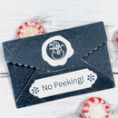 Decorative envelope with a snowman design and 'No Peeking!' text on a white wooden surface.