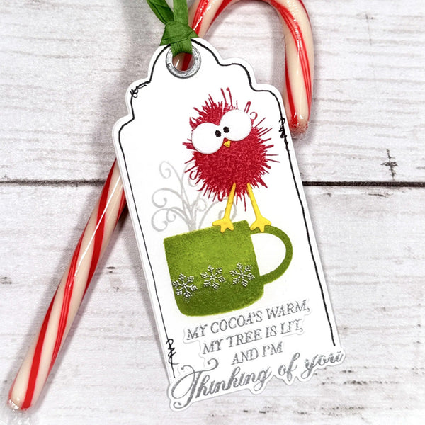Christmas-themed gift tag with a red bird and green mug design, placed on a wooden surface with candy canes.