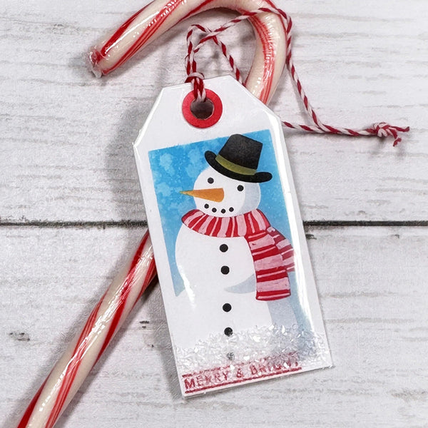 Christmas gift tag with a snowman design on a wooden surface with candy canes.