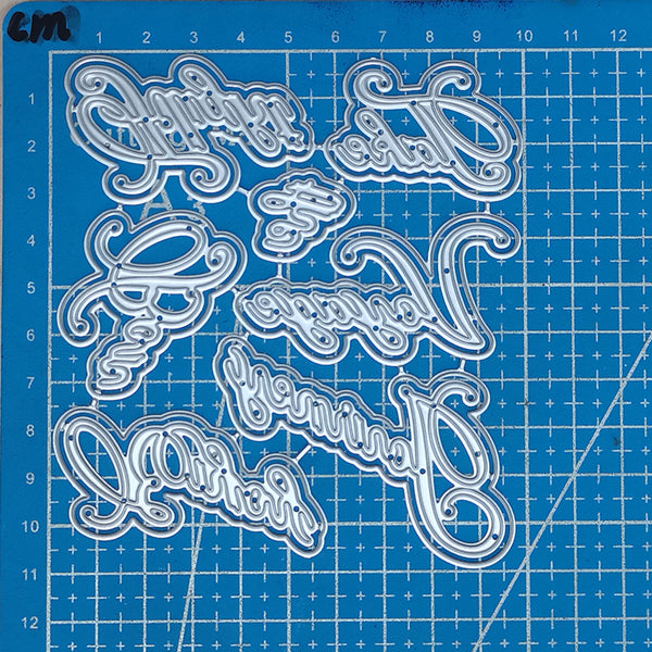 Decorative metal letters on a blue cutting mat with grid lines