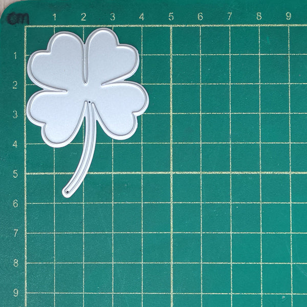 Metallic four-leaf clover on a green cutting mat with grid lines