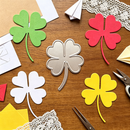 Colorful paper four-leaf clovers on a wooden surface with scissors.