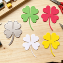 Colorful paper four-leaf clover shapes on a wooden surface with craft supplies.