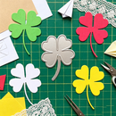 Colorful paper shamrock shapes on a green cutting mat with scissors.