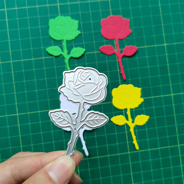 Metal rose stamp held over colored rose cutouts on a green grid background