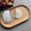 Two metal cutouts of the state of Indiana on a wooden tray with flowers in the background.