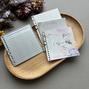 Notebook with different designs on a wooden tray with dried flowers.