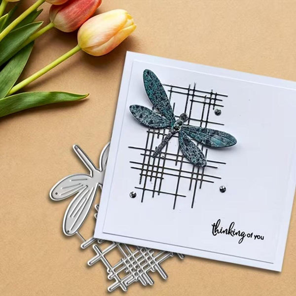 Card with dragonfly design and 'thinking of you' message, surrounded by tulips and metal dragonfly stamps on a beige background.
