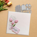 Card with pink tulips and a tag, surrounded by tulip-themed crafting tools on a beige background.