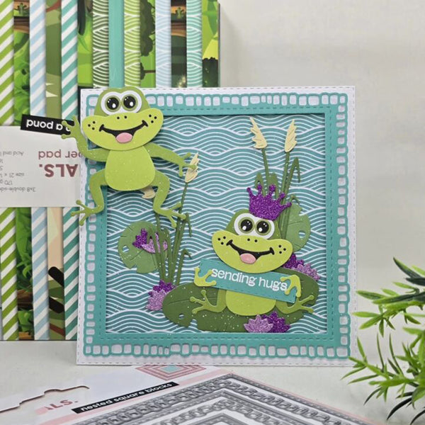Card with two green frogs on a lily pad, surrounded by greenery