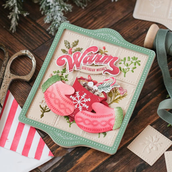 Decorative birthday card with pink mittens and floral elements on a wooden surface.