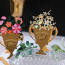 Decorative items shaped like trophies with 'World's Greatest Mom' and 'World's Greatest Dad' text, surrounded by flowers and greenery.