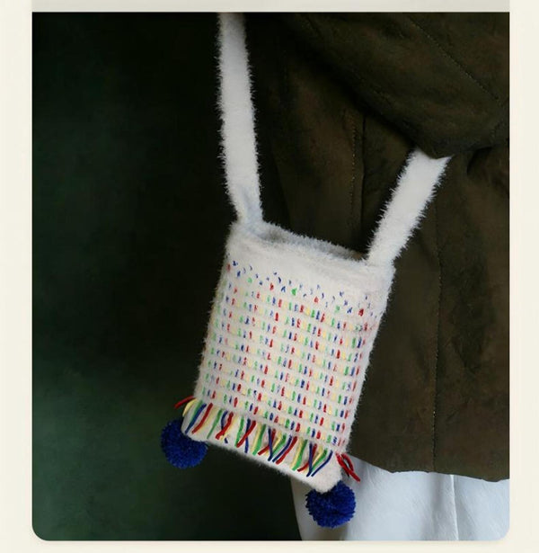 Small bag with colorful pattern and pom-poms attached to a dark coat.