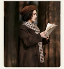 Woman in a brown coat and beret reading a book in a forest setting