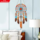 Decorative dreamcatcher with feathers on a light blue wall above a bed.