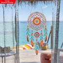 Colorful dreamcatcher hanging by a window with a view of the ocean.