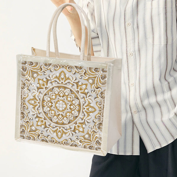 Person holding a decorative tote bag with intricate gold patterns on a white background