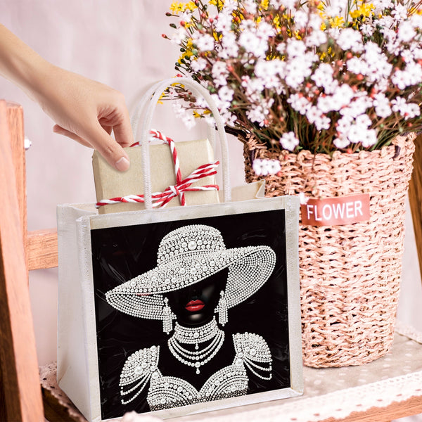 White tote bag with decorative design held by a hand, next to a basket of flowers.