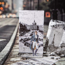Decorative card with a vintage-style illustration of a man in a cityscape, placed on a reflective surface.