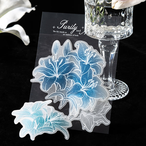 Translucent floral stickers on a black card with a glass of water and white flowers in the background.
