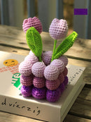 Crocheted purple and pink flowers with green leaves on a wooden surface.