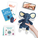 Crocheted elephant toy held by a hand, with crochet pattern book and tools on a white background