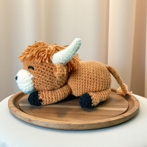 Crocheted toy cow on a wooden tray with a neutral background