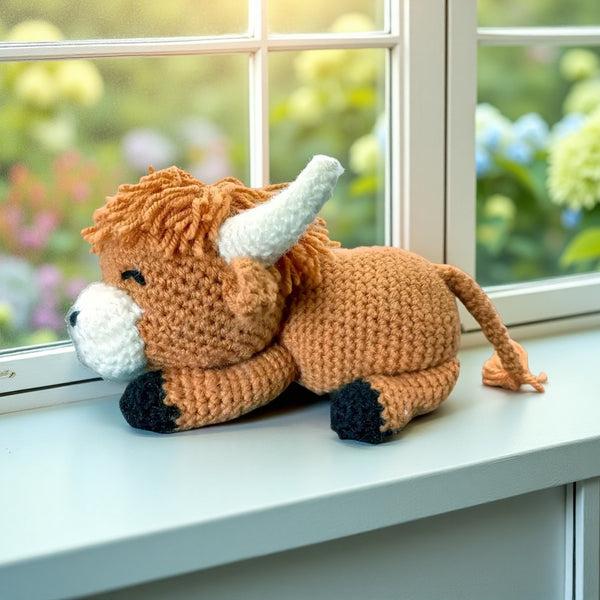 Crocheted bull toy on a windowsill with a garden view
