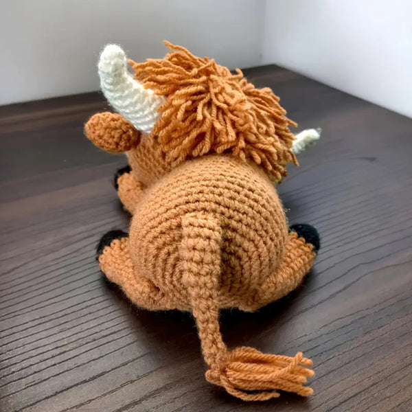 Crocheted toy resembling a highland cow on a wooden surface