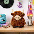 Crocheted Highland cow toy on a shelf with a camera, lava lamp, and records in the background.