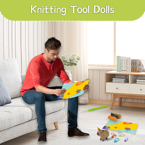 Man sitting on a couch reading a book with knitting tools and dolls on the floor.