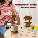 Person crafting a small animal toy with yarn, surrounded by crafting materials on a table.